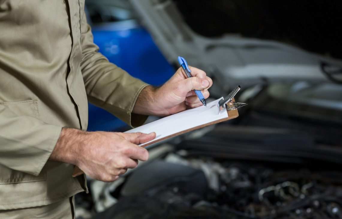 Mid-section of mechanic preparing a check list in repair garage